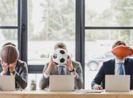 suited men covering their faces with sports balls.