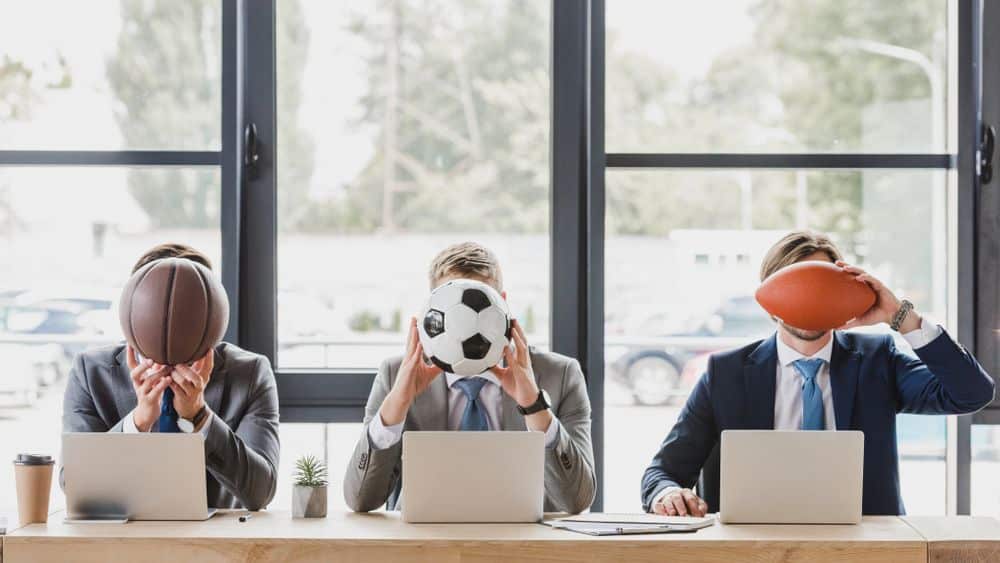 suited men covering their faces with sports balls.