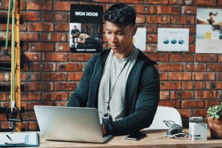 man on his laptop with gym equipment in the background.