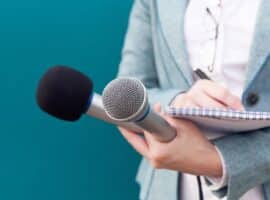 journalist holding two microphones and a notebook