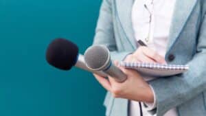 journalist holding two microphones and a notebook