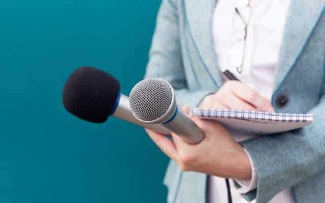journalist holding two microphones and a notebook