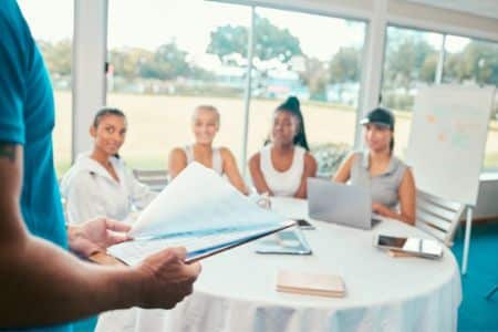 Sports staff attending team meeting with coach reviewing documents