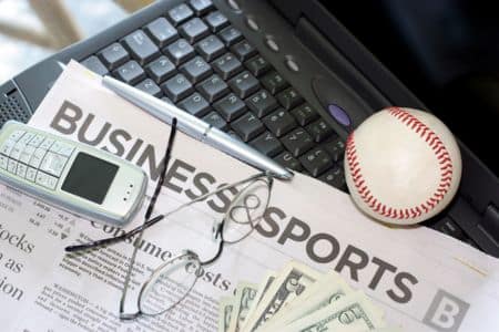 cellphone, glasses, business sports newspaper, and a ball lying on a computer.