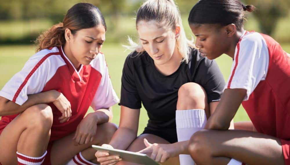 A women's soccer coach huddled with players discussing strategy