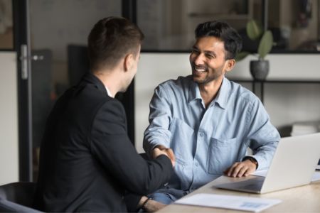 Two men at desk with computer shaking hands