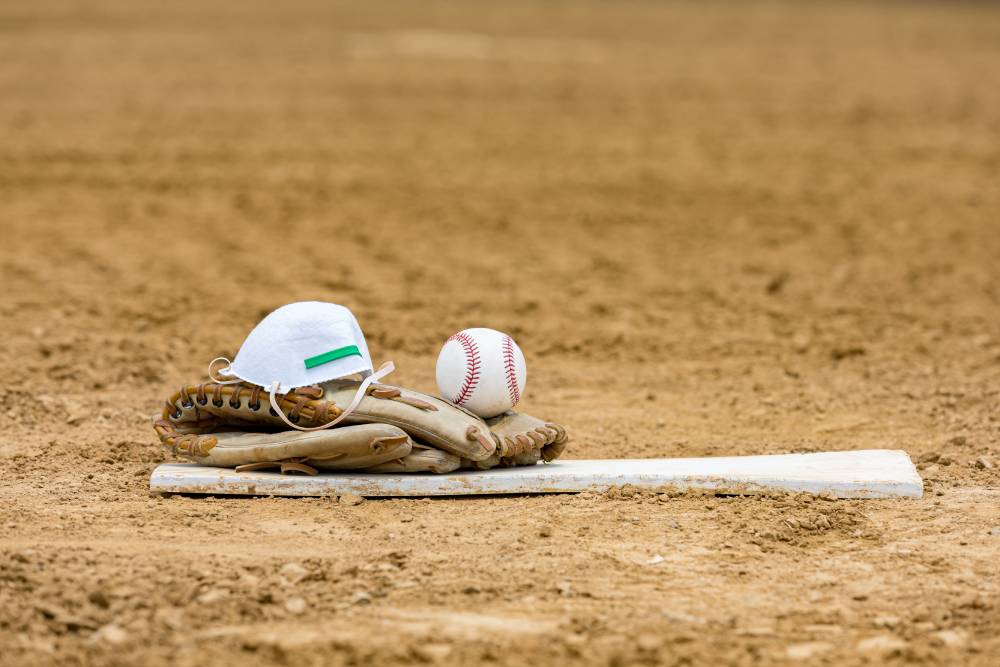 A baseball glove sits on a pitchers mound with a face mask and baseball.