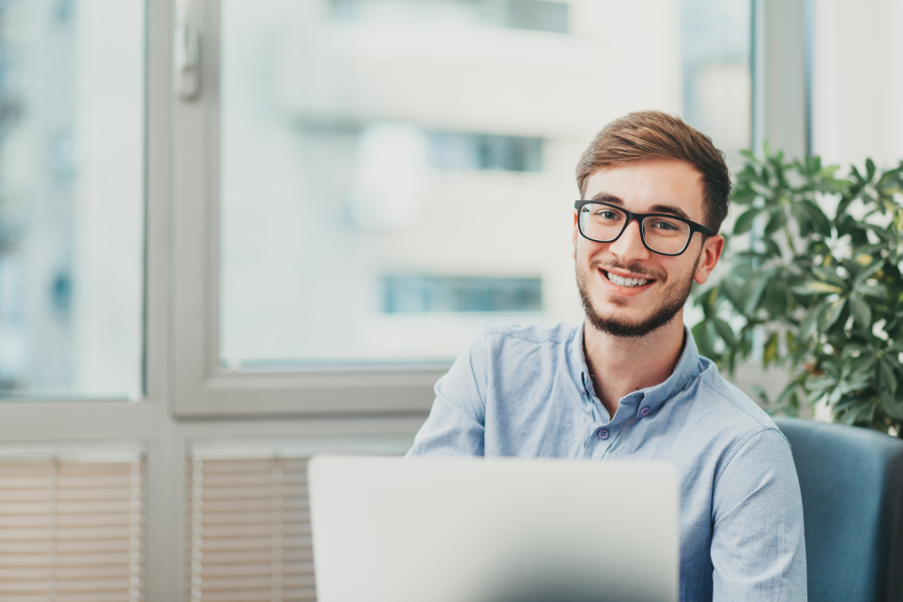 A baseball operations intern smiles from behind a silver laptop as he solves a problem at work.