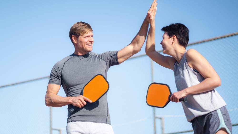 A pickleball instructor giving a high-five to a pickleball student
