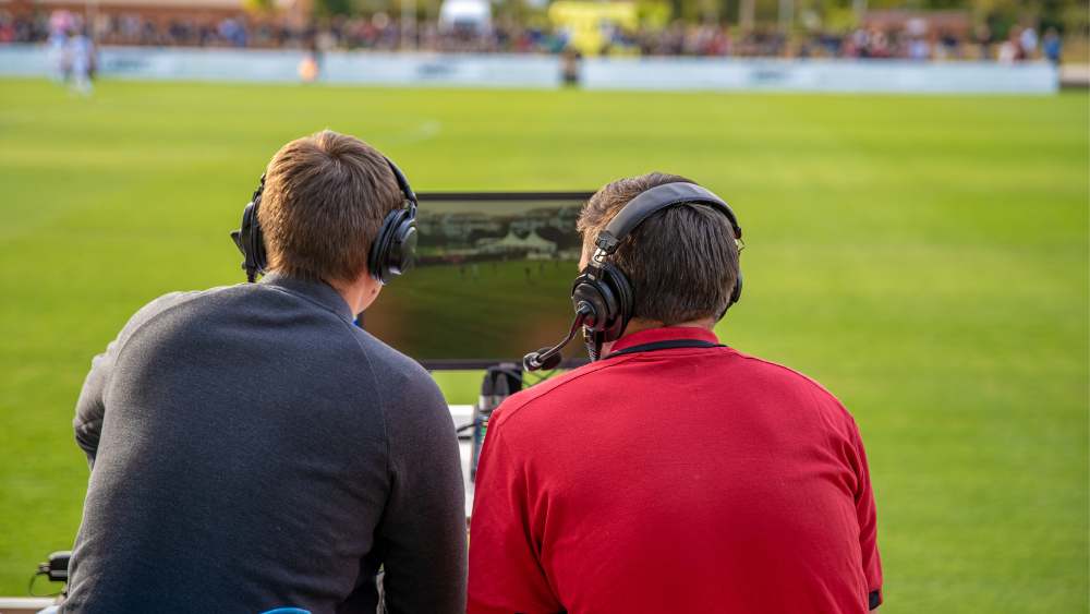 Two sports analysts observing a sports game through a monitor