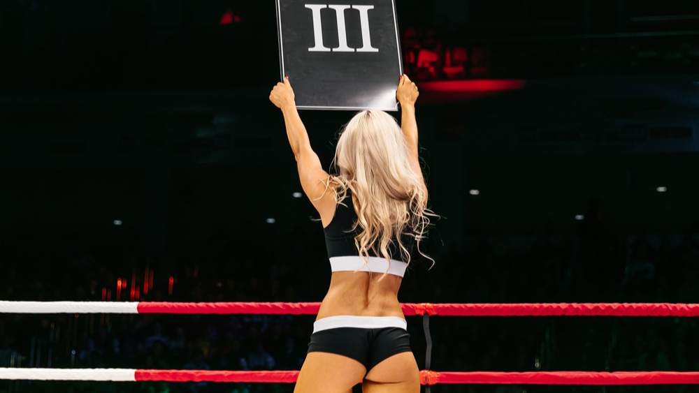 A UFC ring goal holding a sign for round three