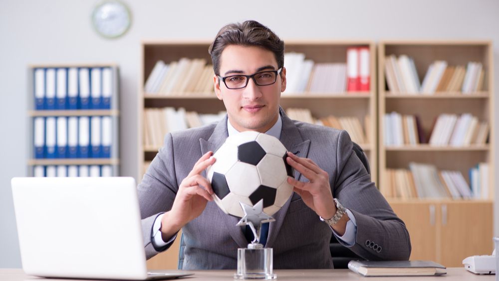 A man in a suit sitting at a desk holding a soccer ball