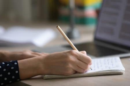 Sports columnist writing in a notebook in front of a laptop