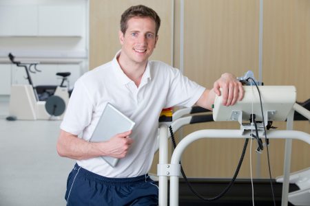 A sports scientist leaning on a treadmill holding a digital tablet in a laboratory.