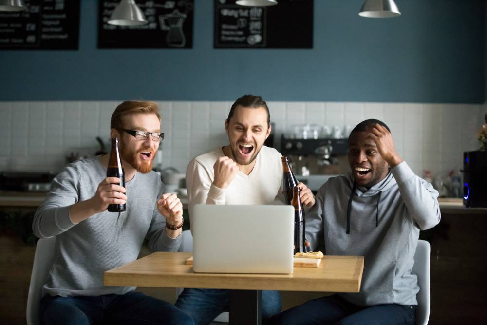 A group of men drink beer while watching the virtual draft on a computer.