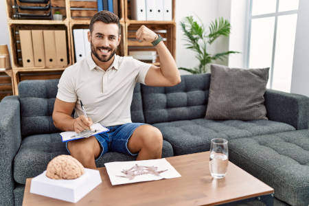 Male volleyball sports psychologist sitting on couch flexing left arm muscle