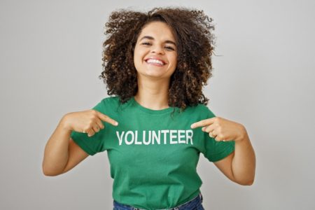 Smiling person pointing to their shirt that says "volunteer"