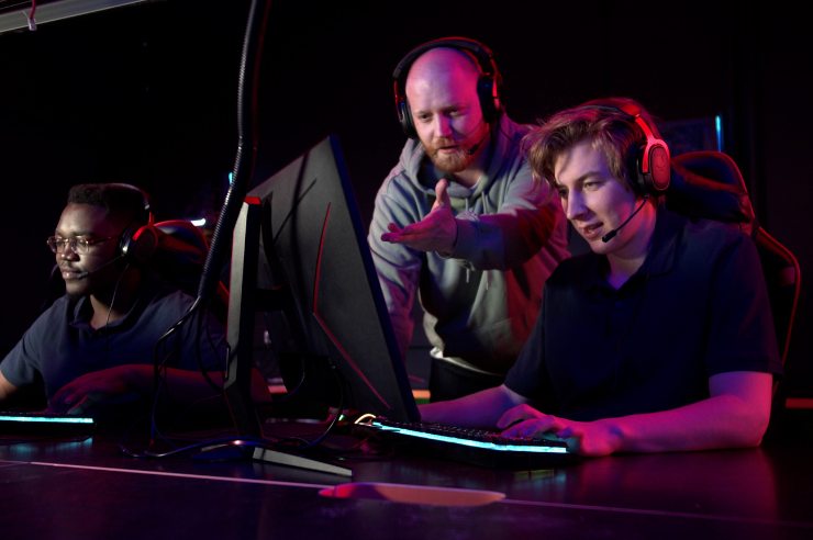 An esports coach guiding an esports team player gaming on a desktop computer.