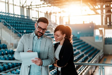 A sports event coordinator planning a sports event with a member of his team in a basketball court.