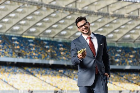 A sports event coordinator standing in a soccer stadium and holding money in his hand.