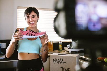 An athlete poses with a shoe in front of a camera for an advertisement belonging to a sports marketing campaign.