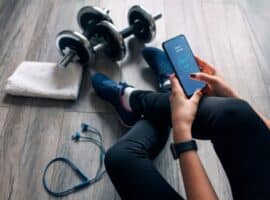 A woman sits while using a fitness app on her smart phone.