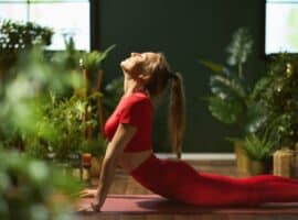 A sports sustainability officer performing yoga on a red yoga mat in a room surrounded by potted plants.