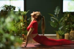 A sports sustainability officer performing yoga on a red yoga mat in a room surrounded by potted plants.