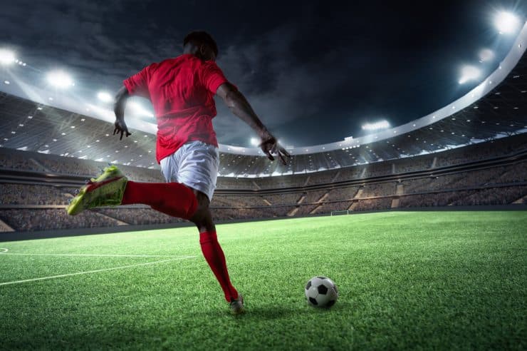 A soccer player prepares to kick a soccer ball inside a soccer stadium during a sports tourism event.