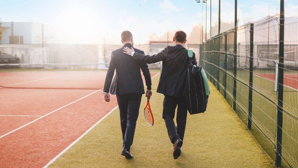 two men carrying tennis gear across the court.