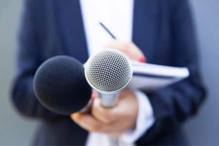 Reporter holding two microphones while writing in their notebook.
