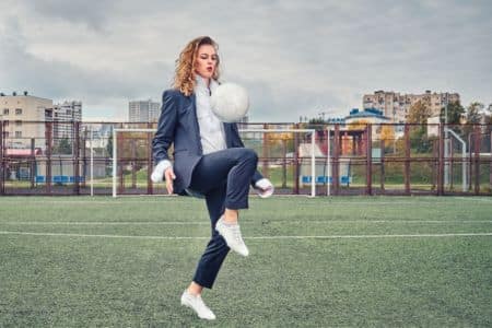 suited woman playing with a soccer ball.