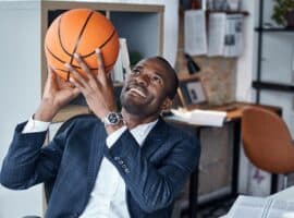 suited man holding a basketball in an office.