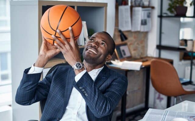 suited man holding a basketball in an office.