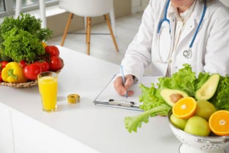 Nutritionist surrounded by vegetables writing on a clipboard.