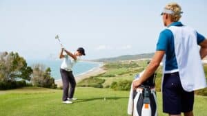golfer teeing off while caddy observes course strategy.