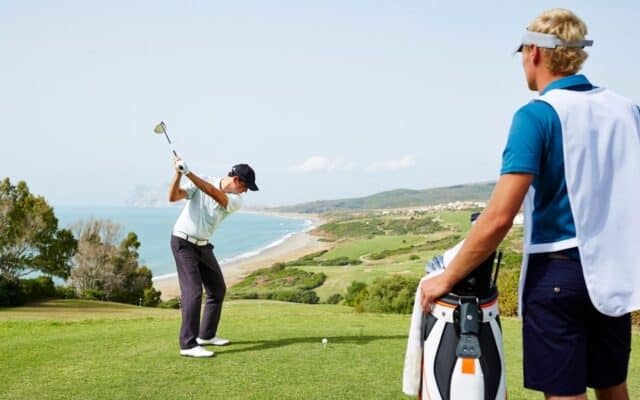 golfer teeing off while caddy observes course strategy.