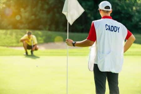 caddie standing by the flagstick while the player lines up a putt.