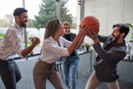 coworkers playfully competing for basketball in a modern office environment.