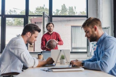 office team collaborating while colleague holds basketball in a corporate setting.