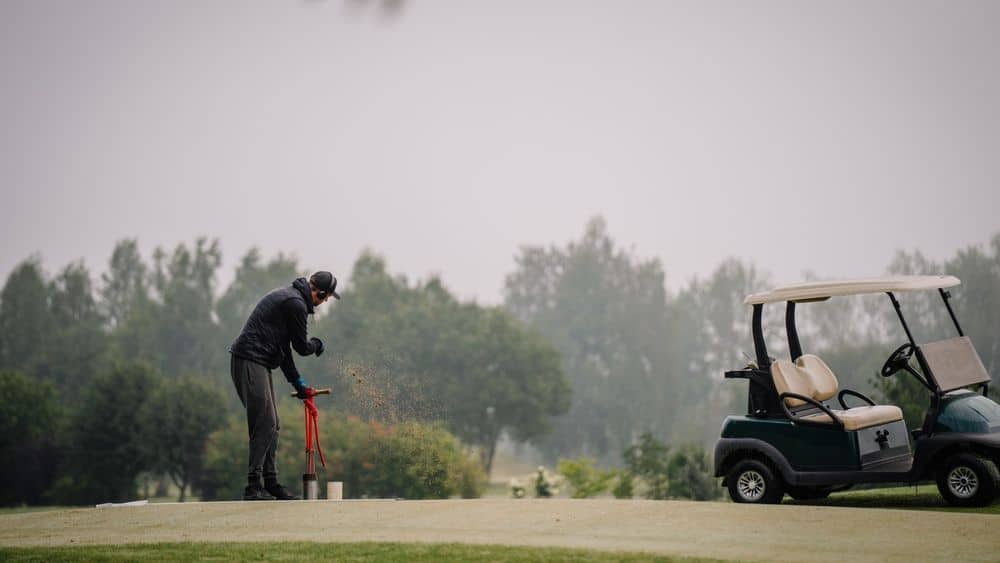 Golf Course Groundskeeper Using Hole Cutter Tool On Foggy Overcast Day
