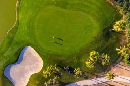 Aerial Drone View Of Lush Golf Course Green With Sand Bunker And Palm Trees