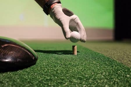 Gloved Hand Carefully Placing Golf Ball On Tee Indoors.