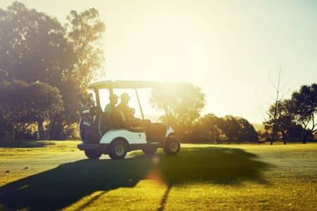 Two Golfers Riding Cart On Bright Sunny Golf Course At Golden Hour