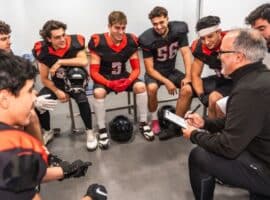 college football coach reviewing strategy with student-athletes before competition