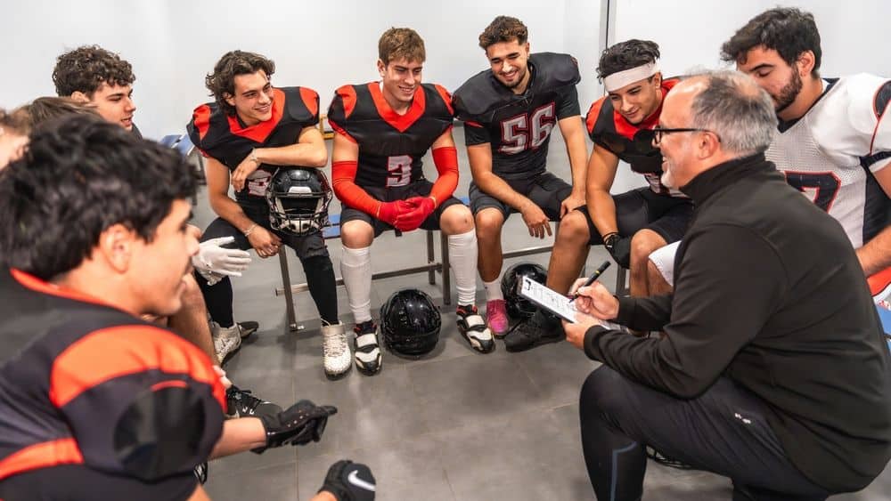 college football coach reviewing strategy with student-athletes before competition